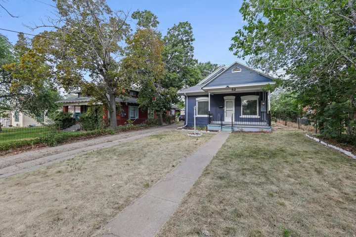 Blue exterior featuring a covered front porch with black wrought iron railing, white trim details, and a front yard with a concrete walkway