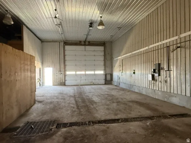 Spacious commercial interior featuring a large 16x16' electric roll-up door, corrugated metal walls and ceiling, concrete flooring with integrated drainage, and overhead lighting fixtures