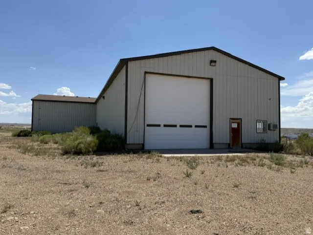 Industrial-style metal building featuring a large white roll-up door, a brown side entry door, and a gable roofline