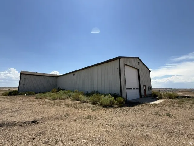 Industrial-style building featuring a large white roll-up door, corrugated metal siding, and a dark-trimmed gable roof