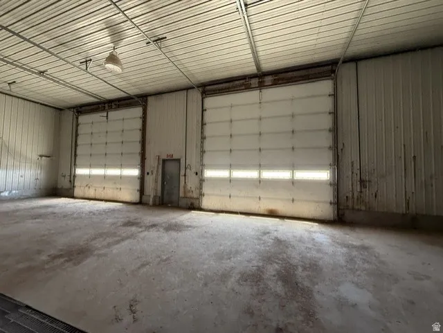 Warehouse interior featuring two large 16x16' electric roll-up doors with window panels, concrete flooring, and an exposed metal ceiling with a suspended light fixture