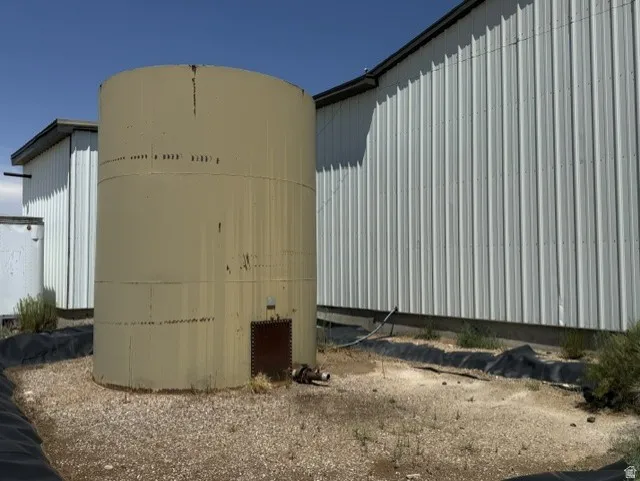 Large cylindrical storage tank on a gravel base, positioned alongside a metal-sided building