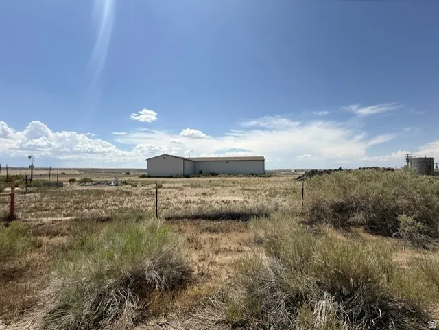 Extensive undeveloped land featuring a large industrial-style building in the distance, surrounded by natural desert vegetation and open skies