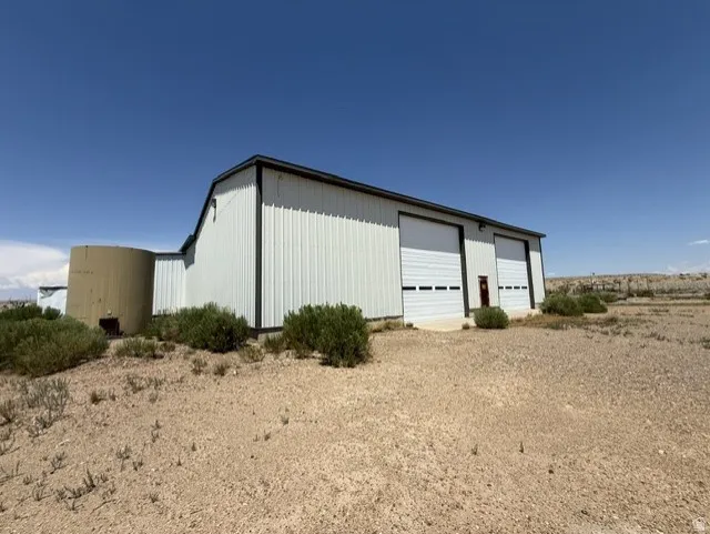 Metal-clad building with two overhead garage doors, a distinct gambrel-style roofline, and an attached cylindrical structure