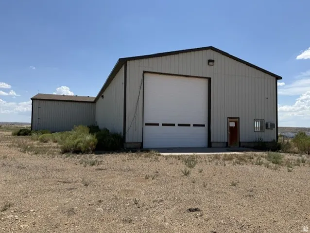 Industrial-style metal building featuring a large white roll-up door, a brown side entry door, and a gable roofline