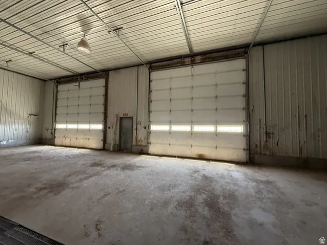 Warehouse interior featuring two large 16x16' electric roll-up doors with window panels, concrete flooring, and an exposed metal ceiling with a suspended light fixture