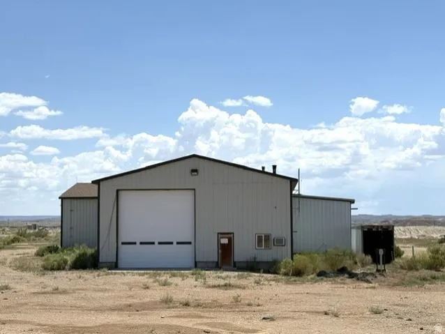 Industrial-style building featuring a large roll-up door, metal siding, and a shingle roof on the attached section