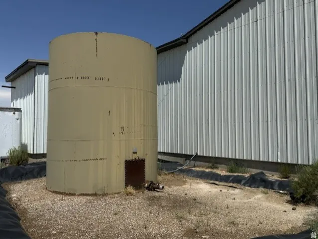 Large cylindrical storage tank on a gravel base, positioned alongside a metal-sided building