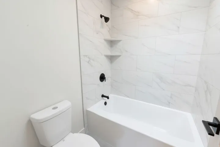 Bathroom featuring a white bathtub, white wall-mounted toilet, and large format marble-look tile surround