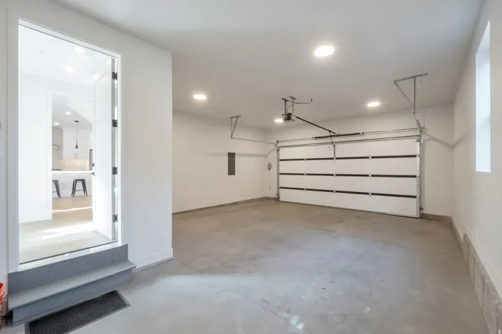 Attached garage featuring a white sectional door, concrete flooring, recessed lighting, and a window for natural light