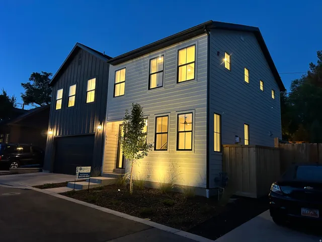 Modern architecture featuring vertical and horizontal siding, multiple windows with dark frames, a dark garage door, and exterior lighting