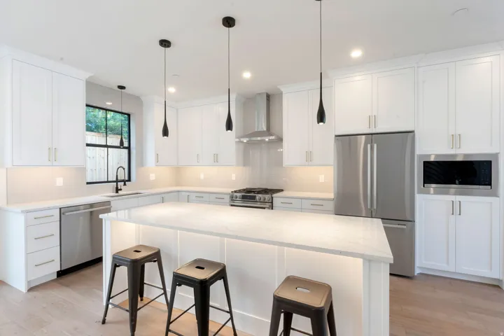 Kitchen featuring white shaker cabinetry, stainless steel appliances, light-toned countertops, pendant lighting, and wood-finish flooring