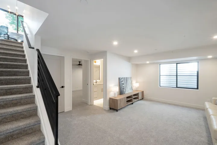 Carpeted staircase with black metal railing, leading to a spacious room with recessed lighting and a large egress window