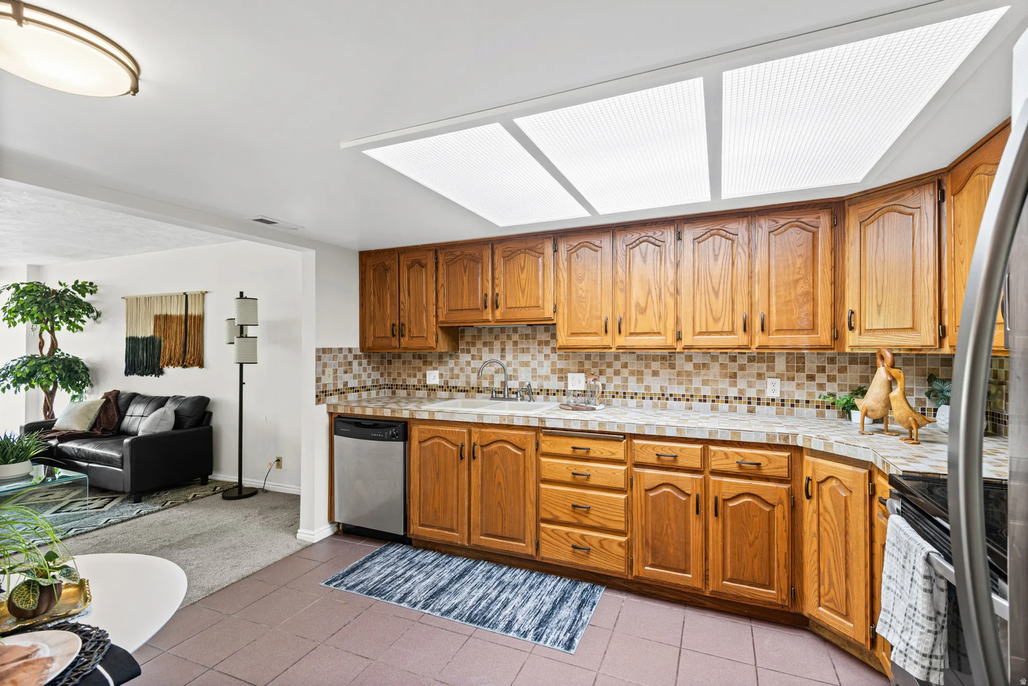 Kitchen featuring light wood cabinetry, a mosaic tile backsplash, and a stainless steel dishwasher