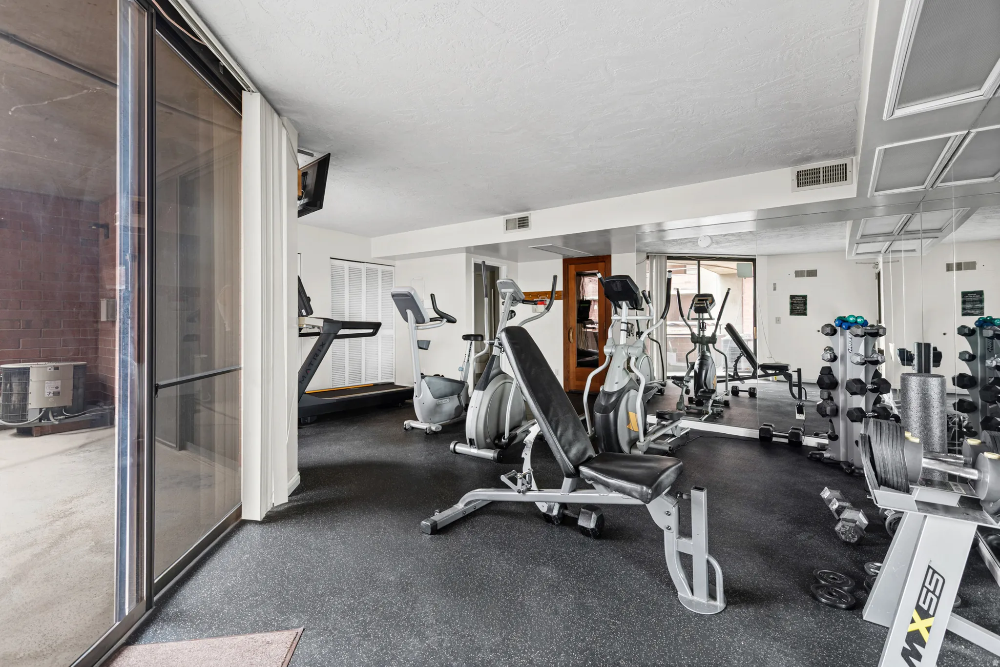 Fitness room featuring resilient rubber flooring, mirrored wall accents, a variety of exercise equipment, and direct access to an outdoor area via sliding glass doors