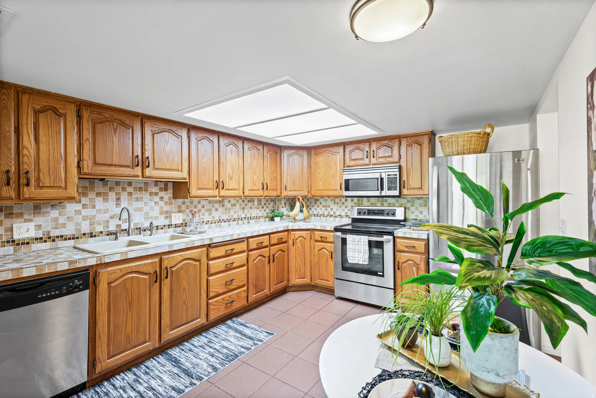Kitchen featuring wood cabinetry, stainless steel appliances, a double basin sink, mosaic tile backsplash, and tile flooring