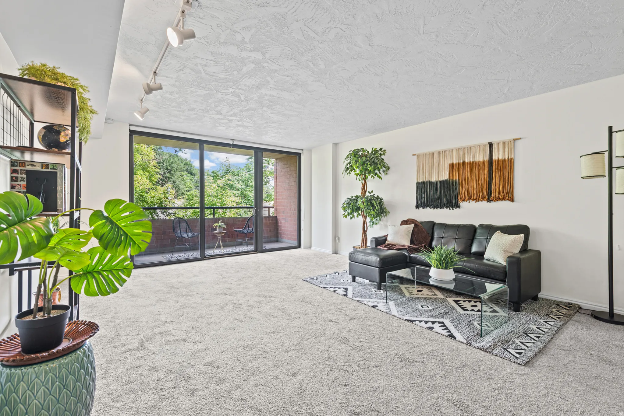 Spacious living area featuring light-colored carpeting and a full-width sliding glass door leading to a private balcony