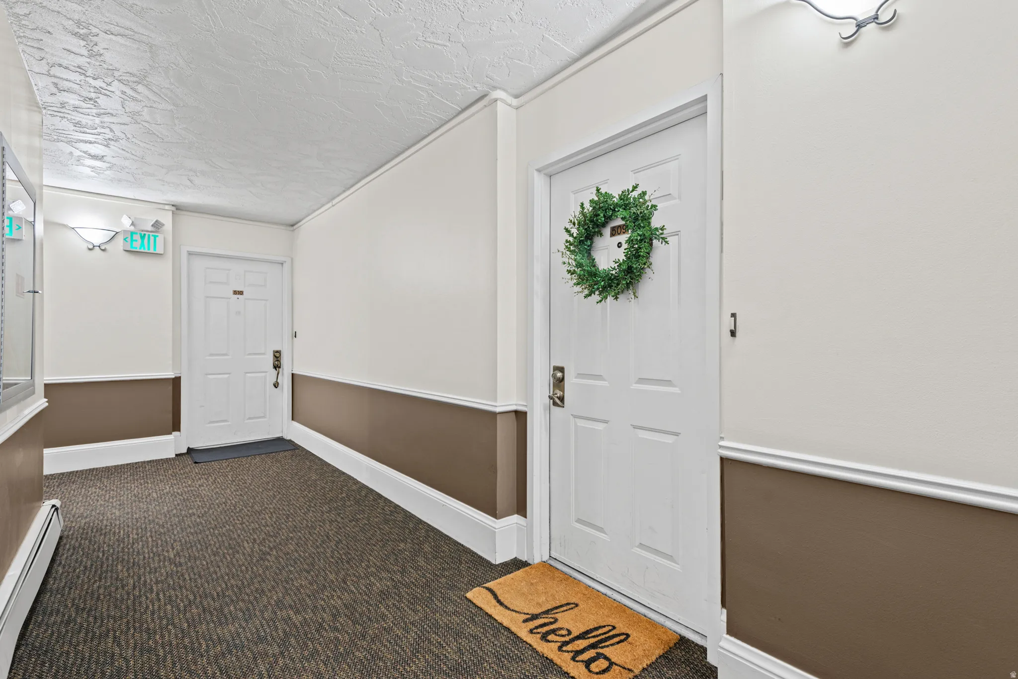 Corridor featuring textured ceiling, wall sconces, patterned carpet, and chair rail molding