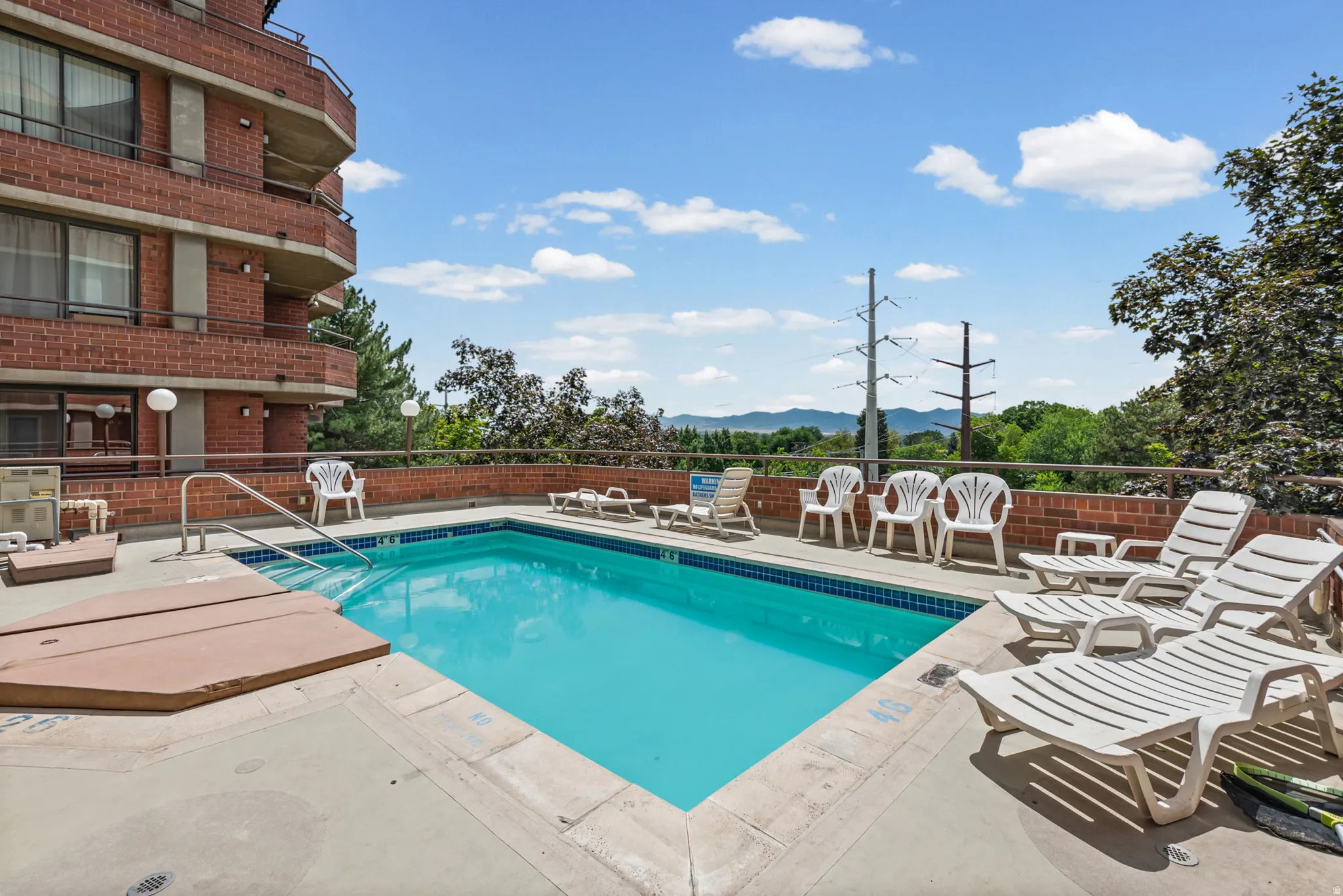 Outdoor swimming pool with integrated hot tub, surrounded by a concrete deck with a brick half-wall