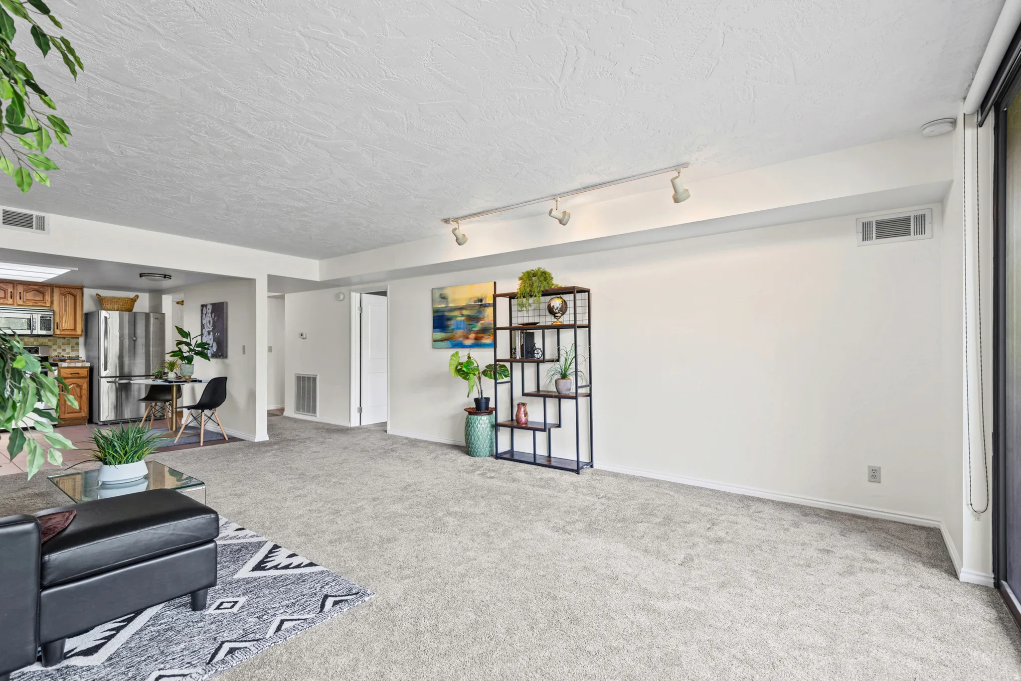 Spacious living area featuring light gray carpeting, track lighting, and a large sliding glass door