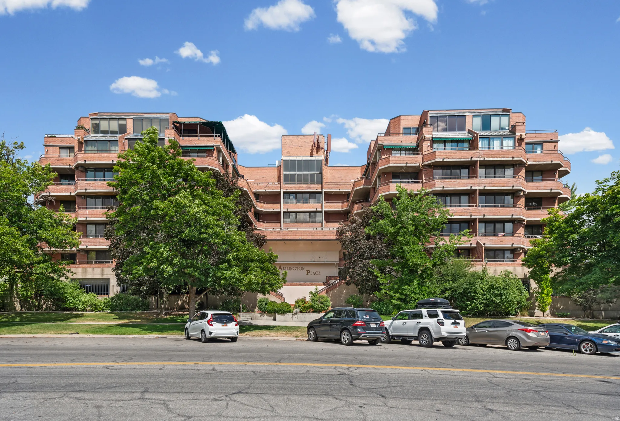 Multi-story brick facade building featuring tiered balconies with dark railings and multiple large windows