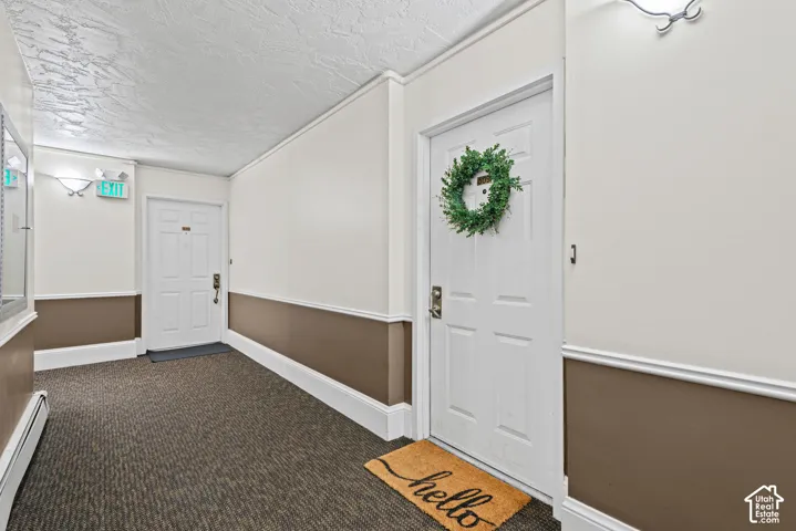 Corridor featuring textured ceiling, wall sconces, patterned carpet, and chair rail molding