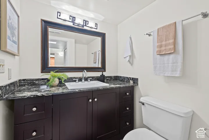 Dark wood-finish vanity with a stone countertop, an integrated rectangular sink, a framed mirror, and a three-light vanity fixture