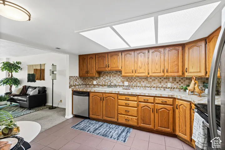 Kitchen featuring light wood cabinetry, a mosaic tile backsplash, and a stainless steel dishwasher