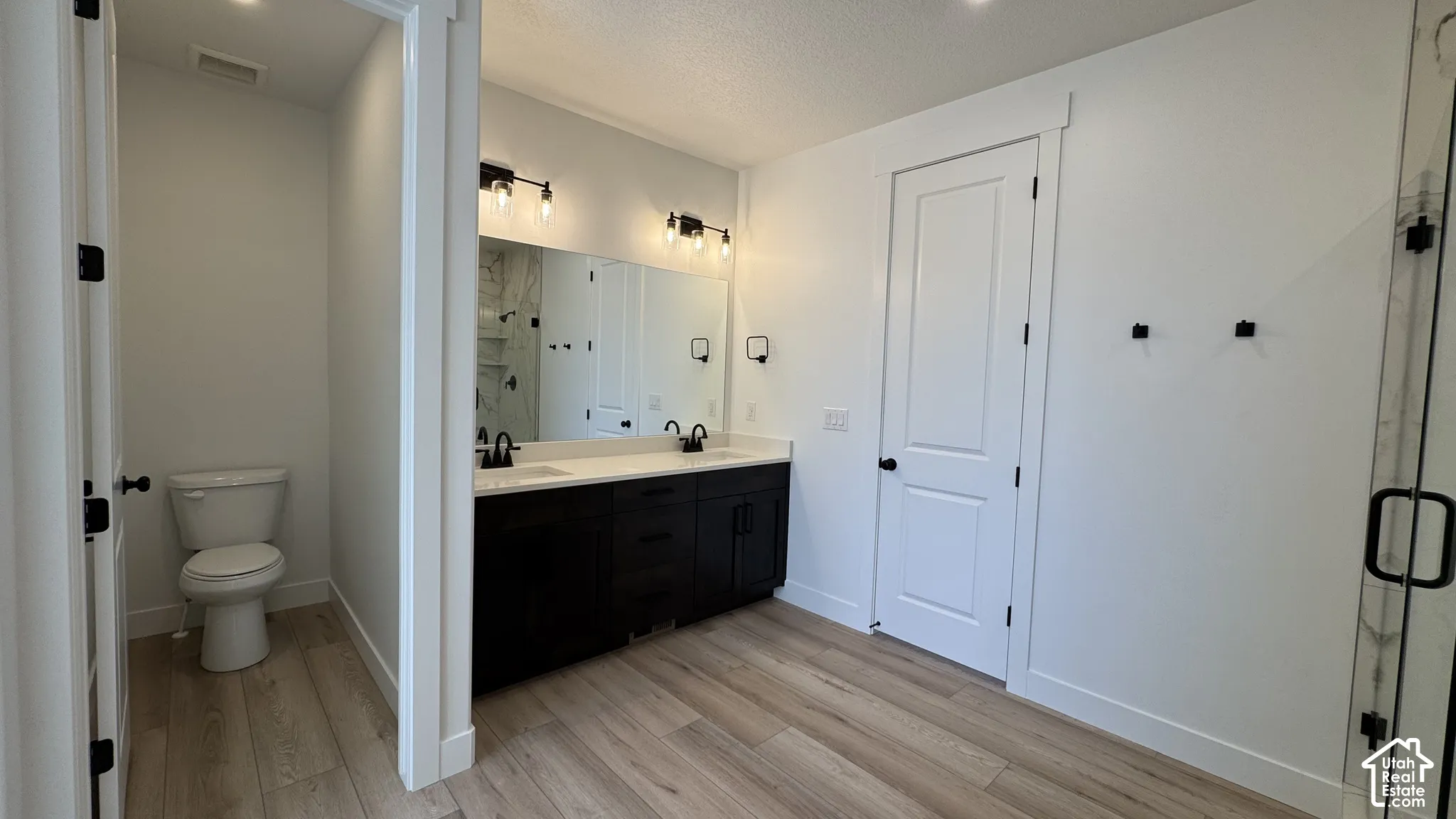 Dual vanity with a white countertop and dark cabinetry, individual mirrors, and wood-finish flooring