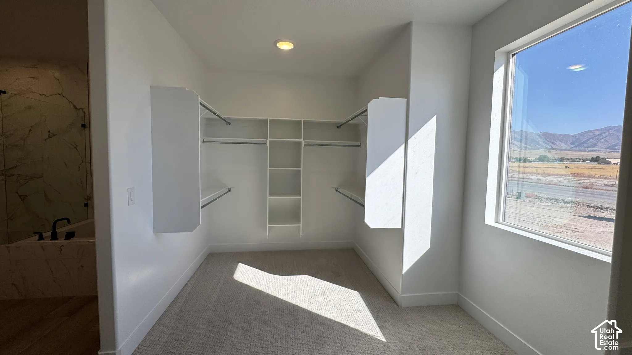 Built-in closet shelving system with hanging rods, recessed ceiling lighting, and a window providing natural light