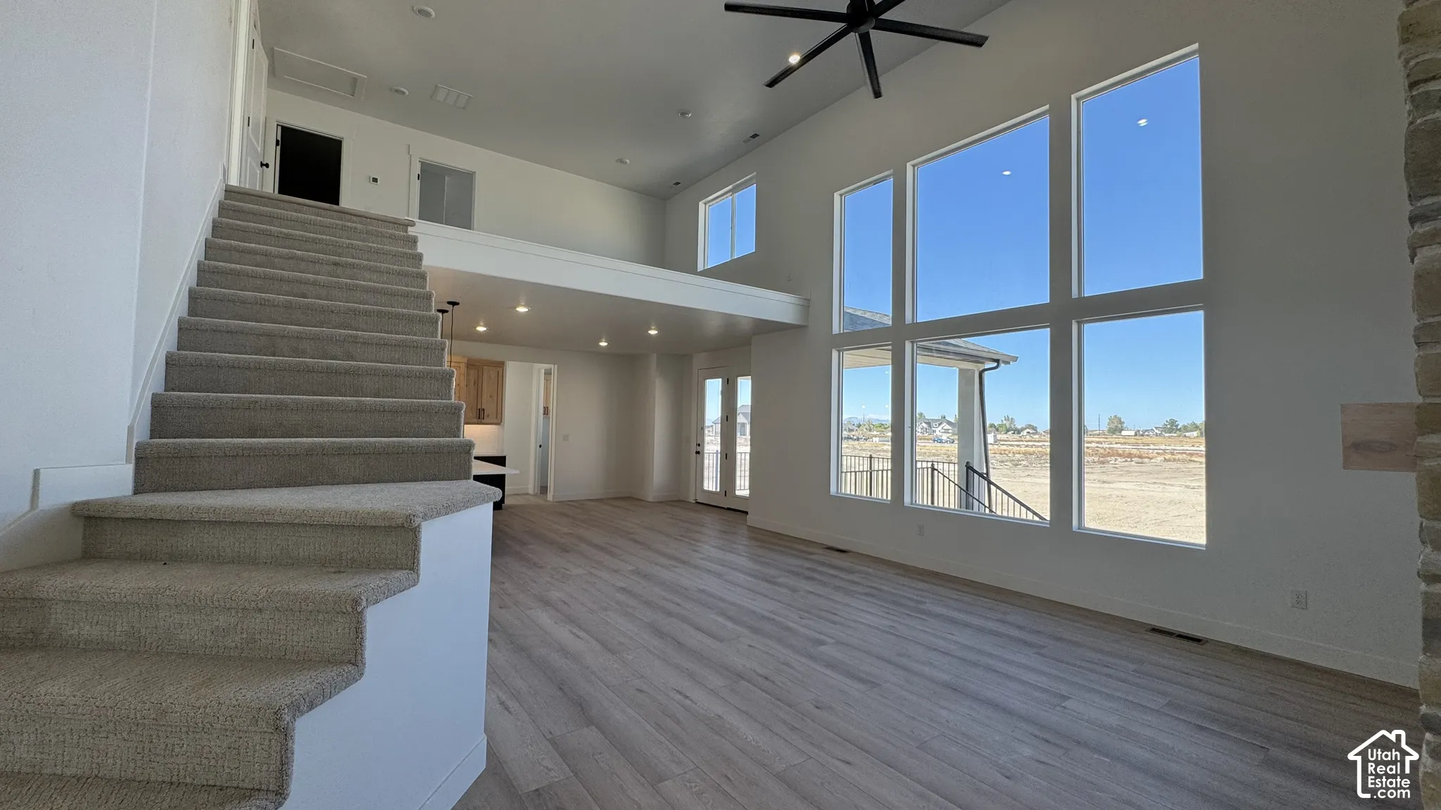 Two-story living area with high ceilings, a wall of large windows, wood-finish flooring, and a carpeted staircase