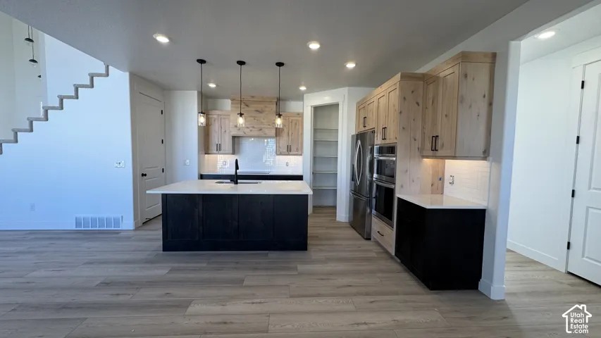 Kitchen featuring wood-finish flooring, a dark wood-finish island with a white countertop, pendant lighting, stainless steel appliances, and white subway tile backsplash