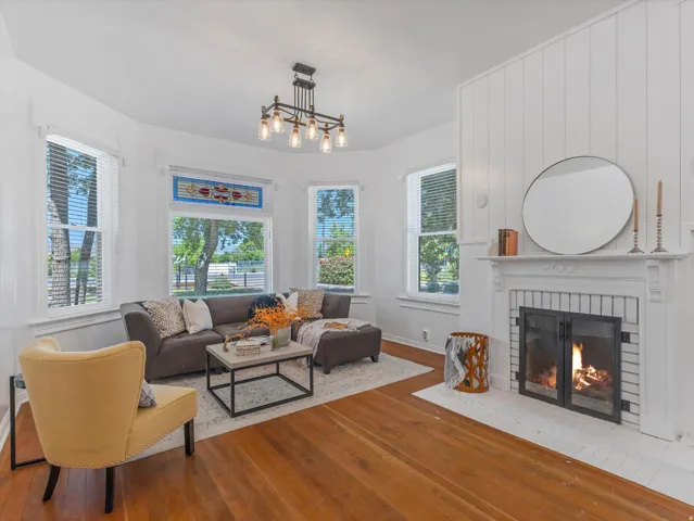 Living area featuring a fireplace with a white brick hearth, wood-finish flooring, and multiple windows