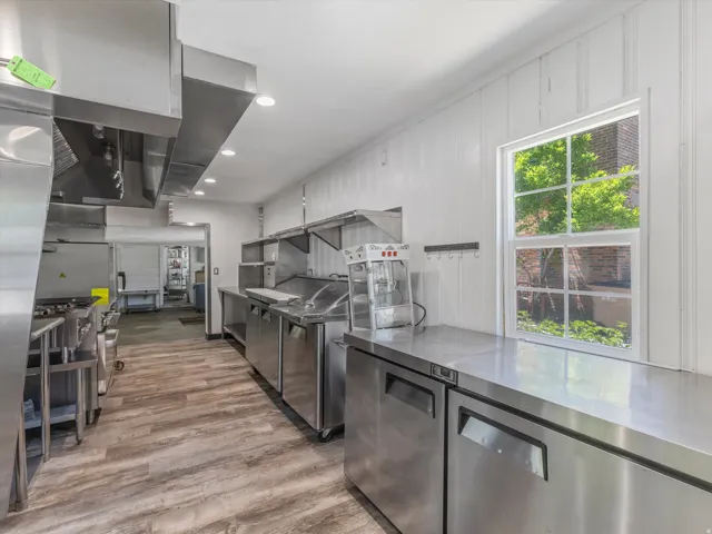 Commercial kitchen featuring extensive stainless steel countertops, professional-grade ventilation hoods, and wood-finish flooring