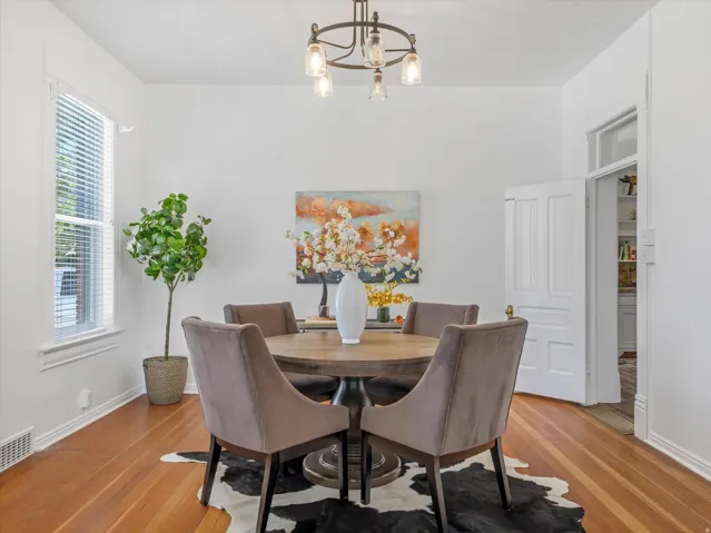 Dining area featuring wood-finish flooring, white baseboards, a window with blinds, a white paneled door, and a multi-bulb chandelier