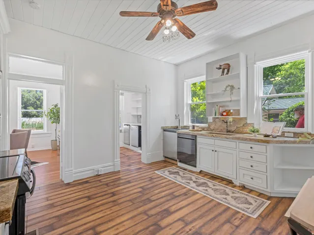 Kitchen featuring wood-finish flooring, white cabinetry, a built-in dishwasher, and granite countertops with a coordinating backsplash