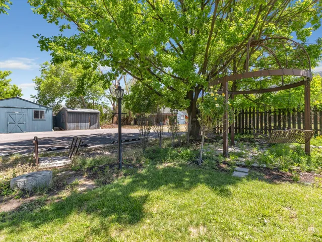 Expansive green lawn featuring a large mature tree, a decorative metal gazebo with a swing, and a black picket fence