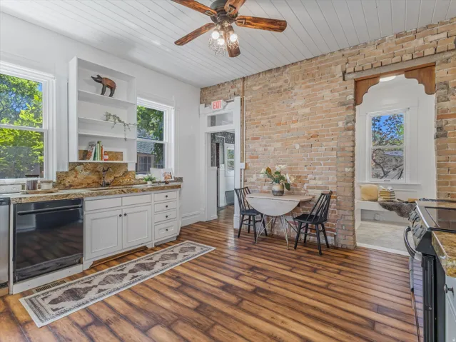 Kitchen featuring wood-finish flooring, exposed brick wall, white cabinetry with stone countertops, and a paneled ceiling with a ceiling fan