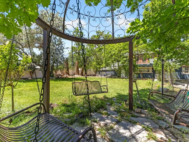 Expansive backyard featuring a central lawn, mature trees, and a decorative metal gazebo with multiple swing seats