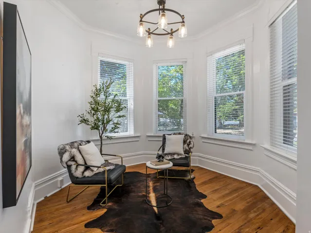Bay window seating area featuring rich wood-finish flooring, white crown molding, and a five-light chandelier