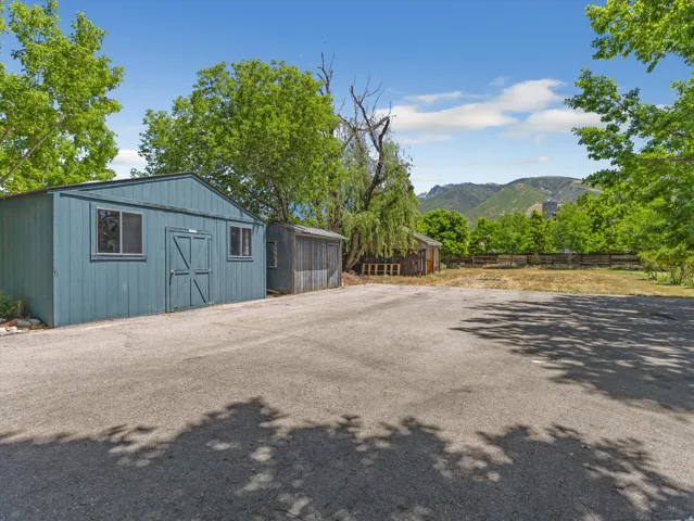 Paved parking area fronting two detached storage buildings, with a fenced level lot and distant mountains