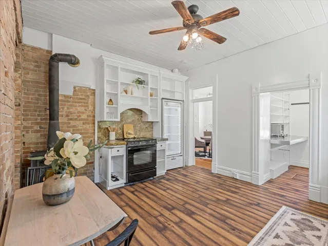 Open-concept living space featuring wood-finish flooring, a white beadboard ceiling, and a rustic wood-burning stove