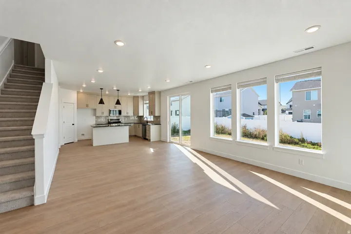 Open-concept living space with wood-finish flooring, a contemporary kitchen featuring an island and stainless steel appliances, recessed lighting, and a sliding glass door to the exterior