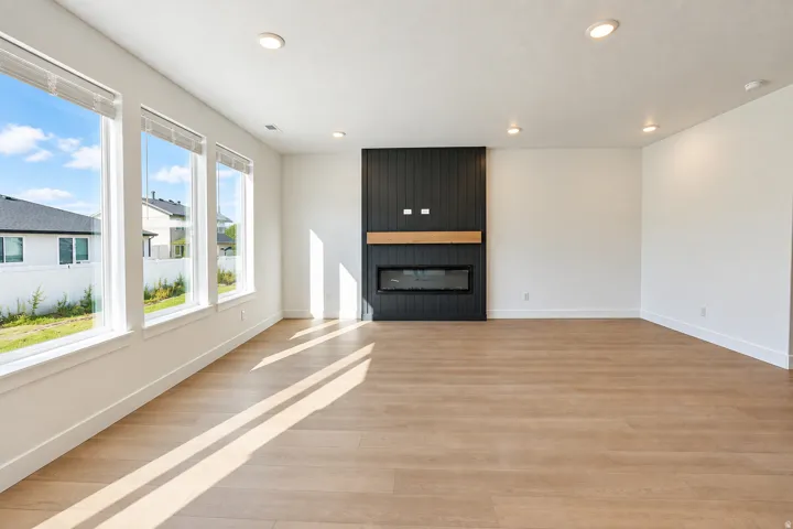 Spacious living area featuring wood-finish flooring, a modern fireplace with a dark paneled surround, a light wood mantel, and multiple large windows