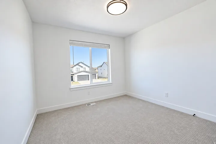 Neutral wall color, carpet flooring, window with white trim, and a flush-mount ceiling light