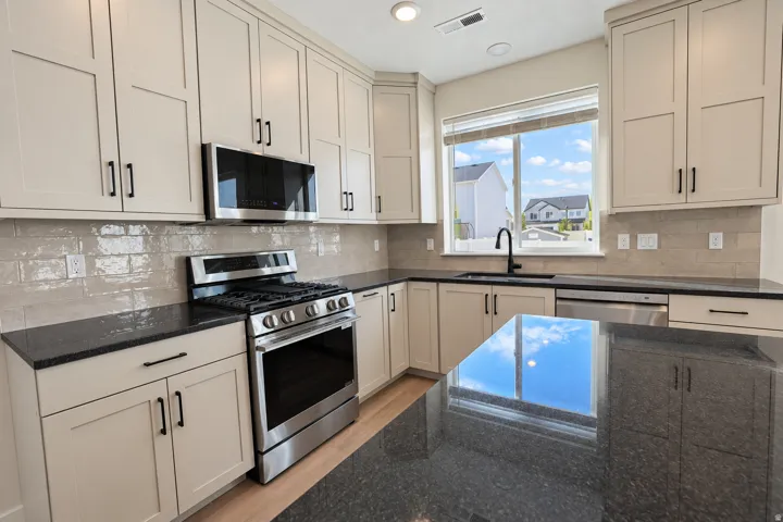 Kitchen featuring light-toned cabinetry, dark countertops, stainless steel appliances, a tile backsplash, and a central island