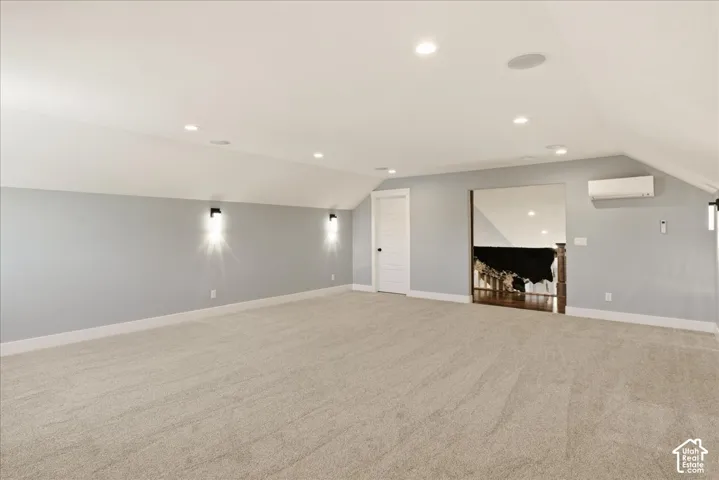 Spacious carpeted room featuring recessed lighting, wall-mounted sconces, a built-in speaker system, and a mini-split climate control unit