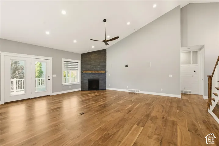 Spacious room featuring wood-finish flooring, a contemporary fireplace with a stone surround and wood mantel, and soaring vaulted ceilings