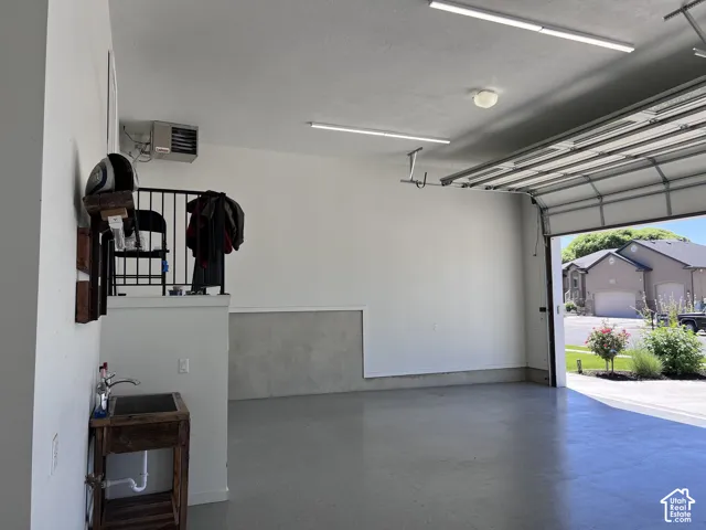 main garage Spacious garage featuring a finished concrete floor, overhead lighting, an exposed garage door track system, an integrated utility sink, and a wall-mounted heating unit