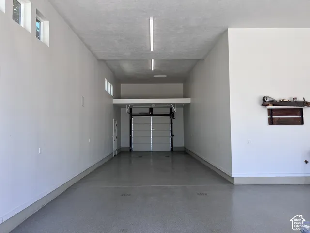main garage - Spacious garage featuring a full-width overhead door, high ceilings, a durable epoxy floor finish, and integrated linear lighting